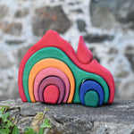 The Glückskäfer Gable House wooden toy placed on a stone wall outdoors. The set has 9 wooden pieces that fit together snuggly to form the complete red gable house.
