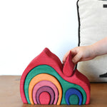 A child placing the smallest red piece onto the Glückskäfer Gable House wooden toy. 