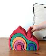 A child placing the smallest red piece onto the Glückskäfer Gable House wooden toy. 