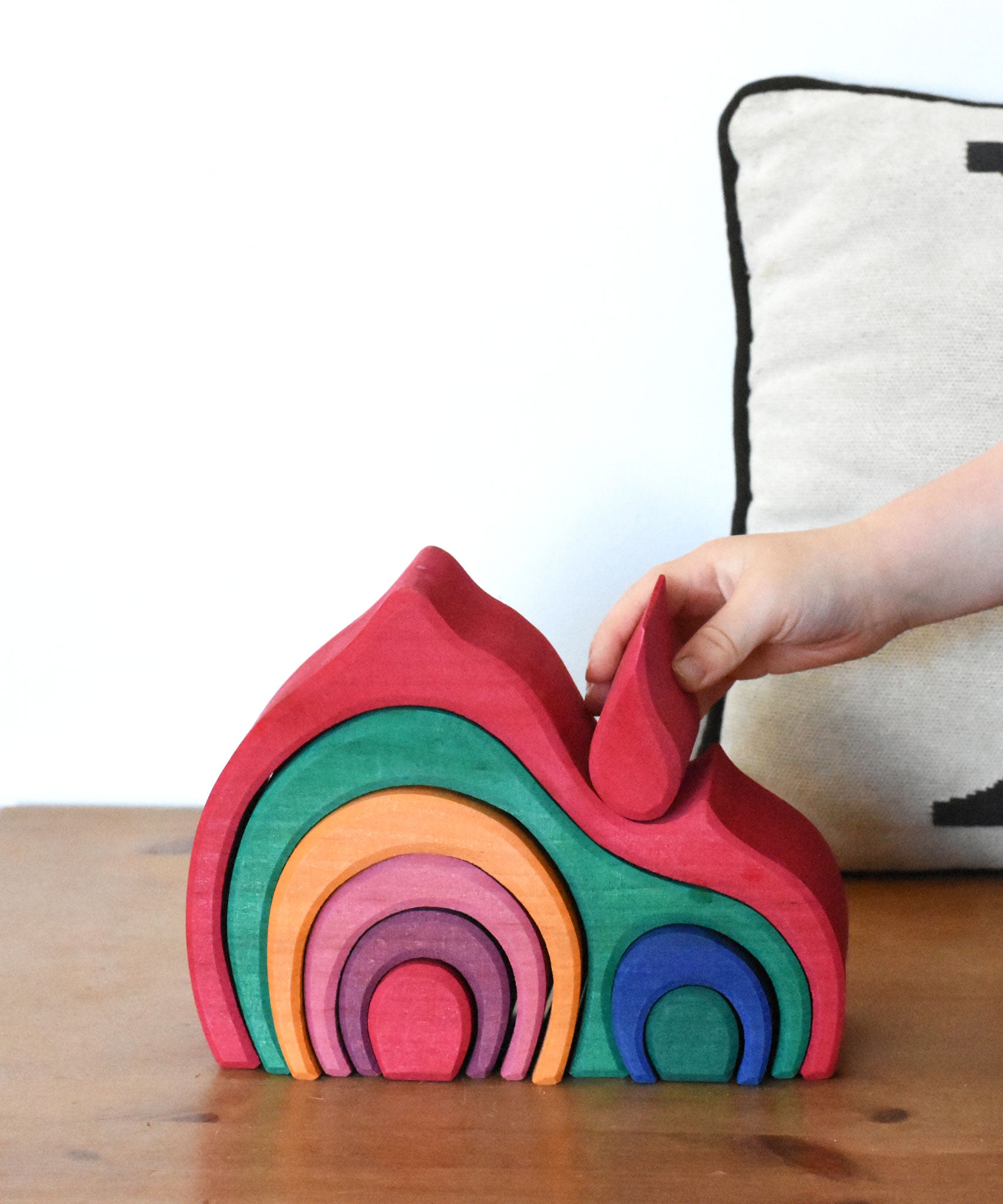 A child placing the smallest red piece onto the Glückskäfer Gable House wooden toy. 