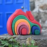 The Glückskäfer Gable House 9 Piece Wooden Toy placed on a stone wall outdoors. 
