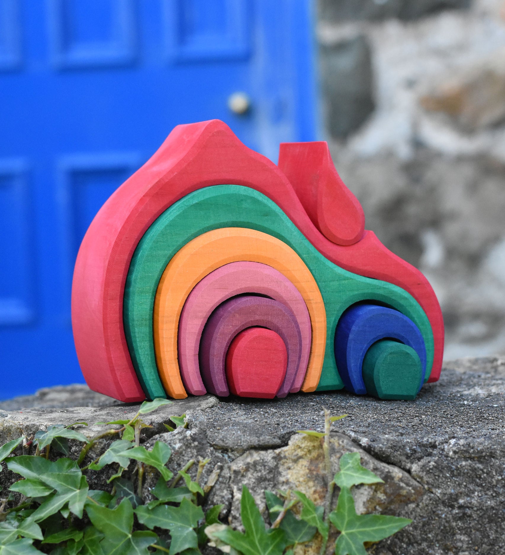 The Glückskäfer Gable House 9 Piece Wooden Toy placed on a stone wall outdoors. 