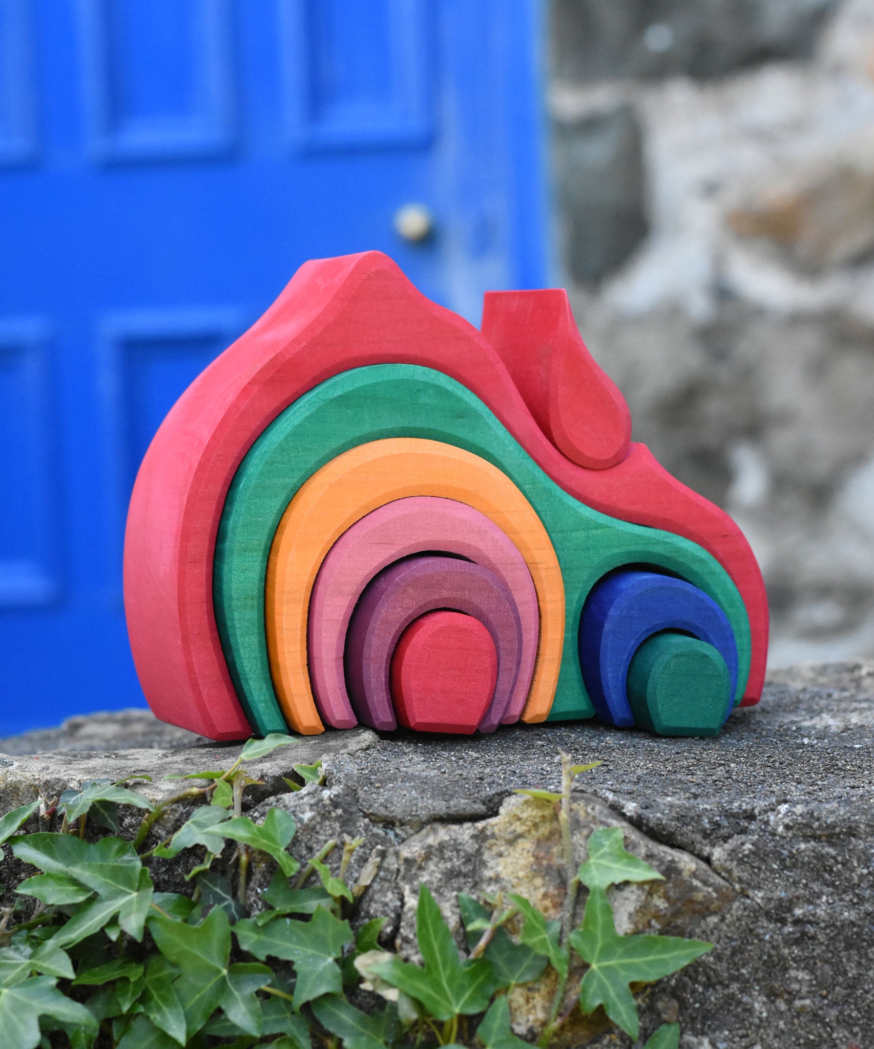 The Glückskäfer Gable House 9 Piece Wooden Toy placed on a stone wall outdoors. 