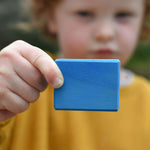 A child holding up a blue block from the Glückskäfer 29-Piece House Blocks set.