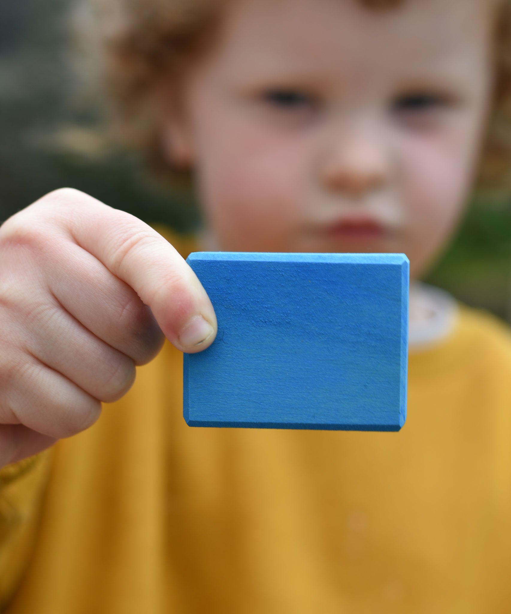 A child holding up a blue block from the Glückskäfer 29-Piece House Blocks set.