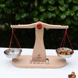 Glückskäfer balance with weights children's weighing scales toy placed on a table outdoors with a weight on one side and Grapat mandala mushroom pieces.  