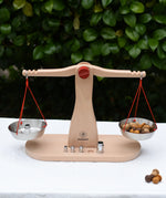 Glückskäfer balance with weights children's weighing scales toy placed on a table outdoors with a weight on one side and Grapat mandala mushroom pieces.  