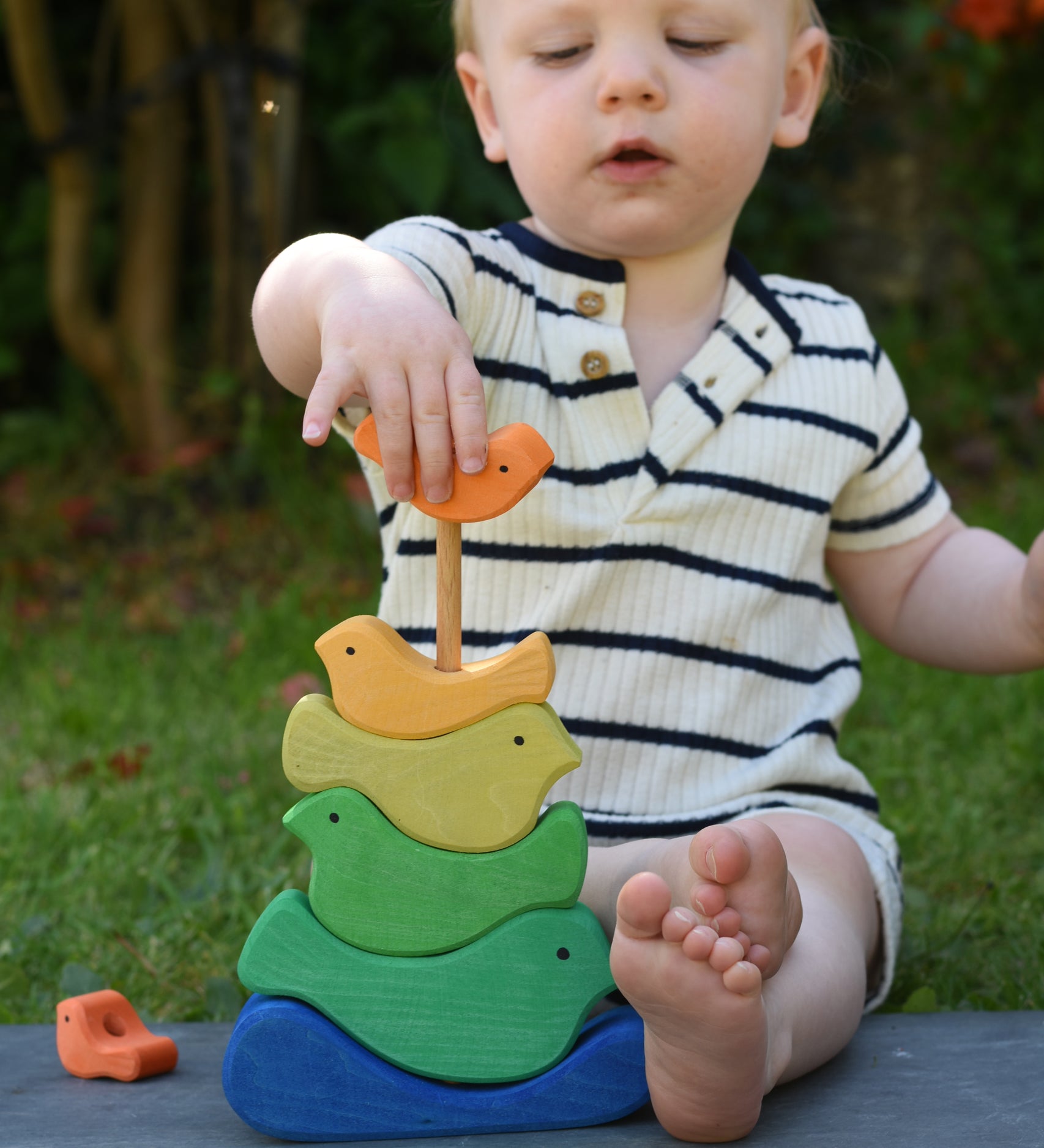 A child playing with the Glückskäfer Bird Stacker placing one of the orange coloured birds onto the stack. 