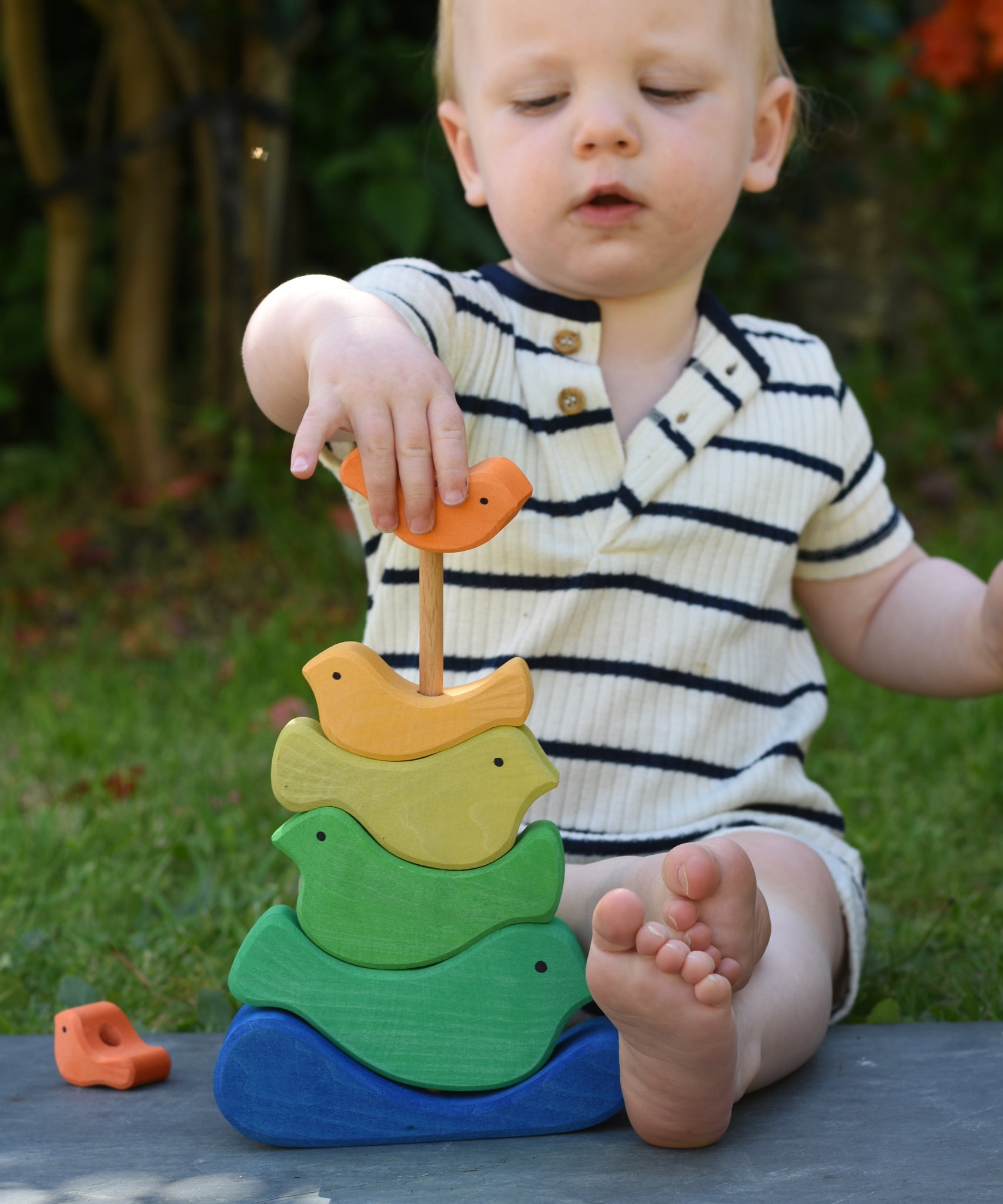 A child playing with the Glückskäfer Bird Stacker placing one of the orange coloured birds onto the stack. 