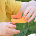 A yellow and orange bird from the Glückskäfer Bird Stacker in a child's hands.
