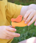 A yellow and orange bird from the Glückskäfer Bird Stacker in a child's hands.