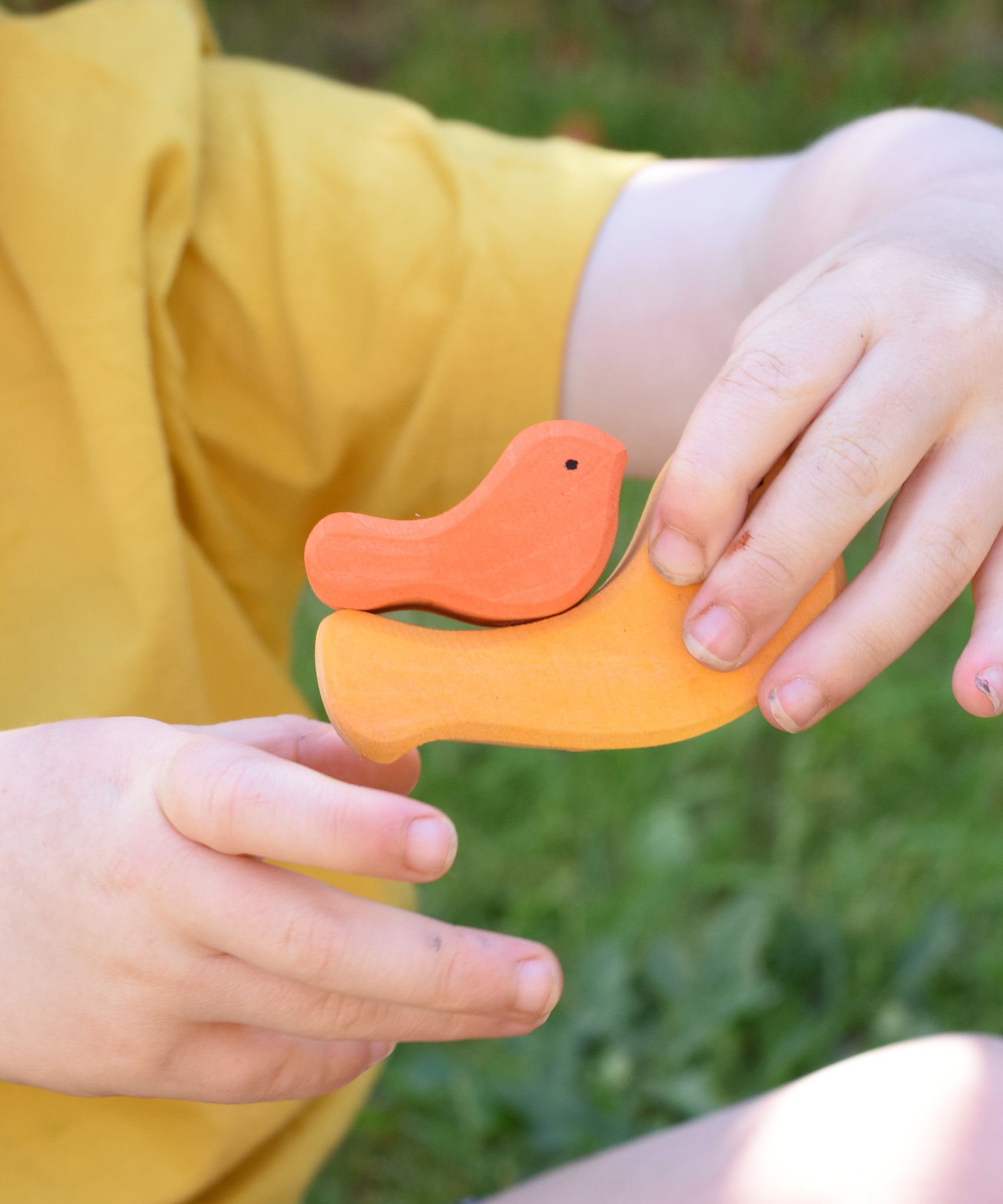 A yellow and orange bird from the Glückskäfer Bird Stacker in a child's hands.