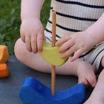 A close up of a child's hands placing the green coloured bird onto the pole on the base of the Glückskäfer Bird Stacker.
