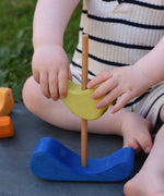 A close up of a child's hands placing the green coloured bird onto the pole on the base of the Glückskäfer Bird Stacker.