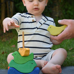 A close up of an adult's hand handing a green coloured bird piece over to a child which is playing with the Glückskäfer Bird Stacker.