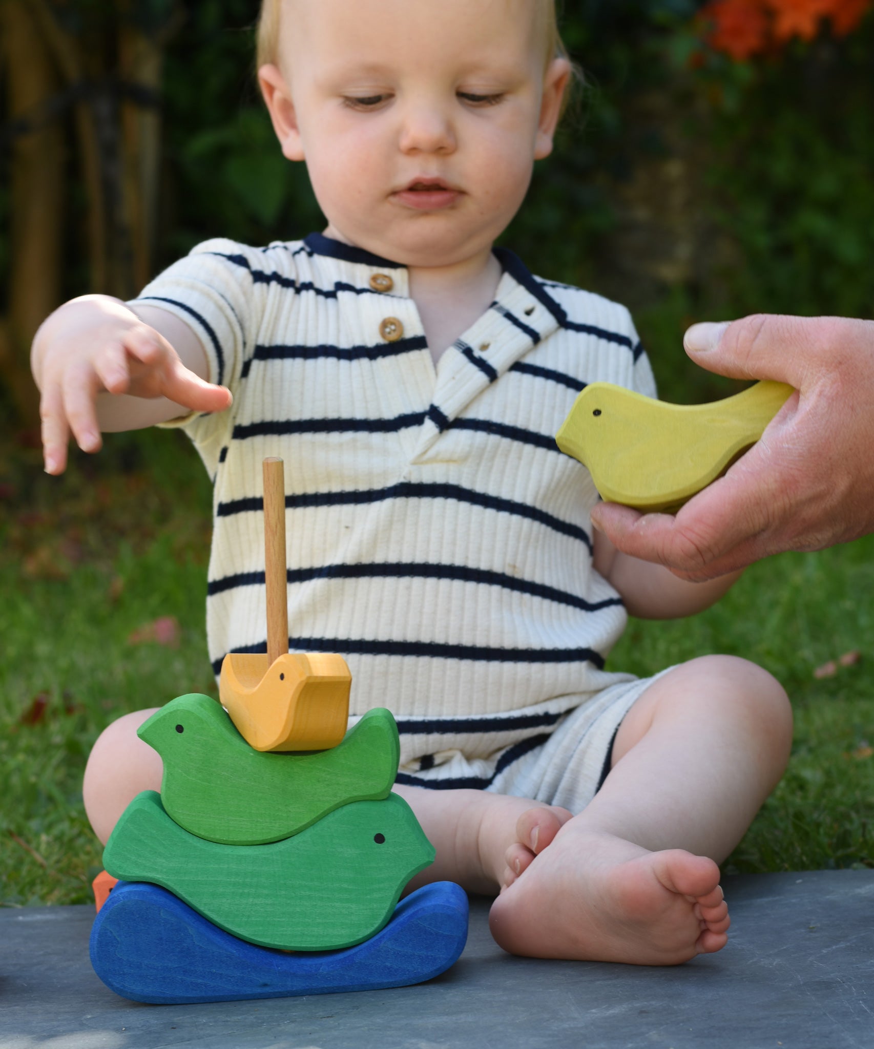 A close up of an adult's hand handing a green coloured bird piece over to a child which is playing with the Glückskäfer Bird Stacker.