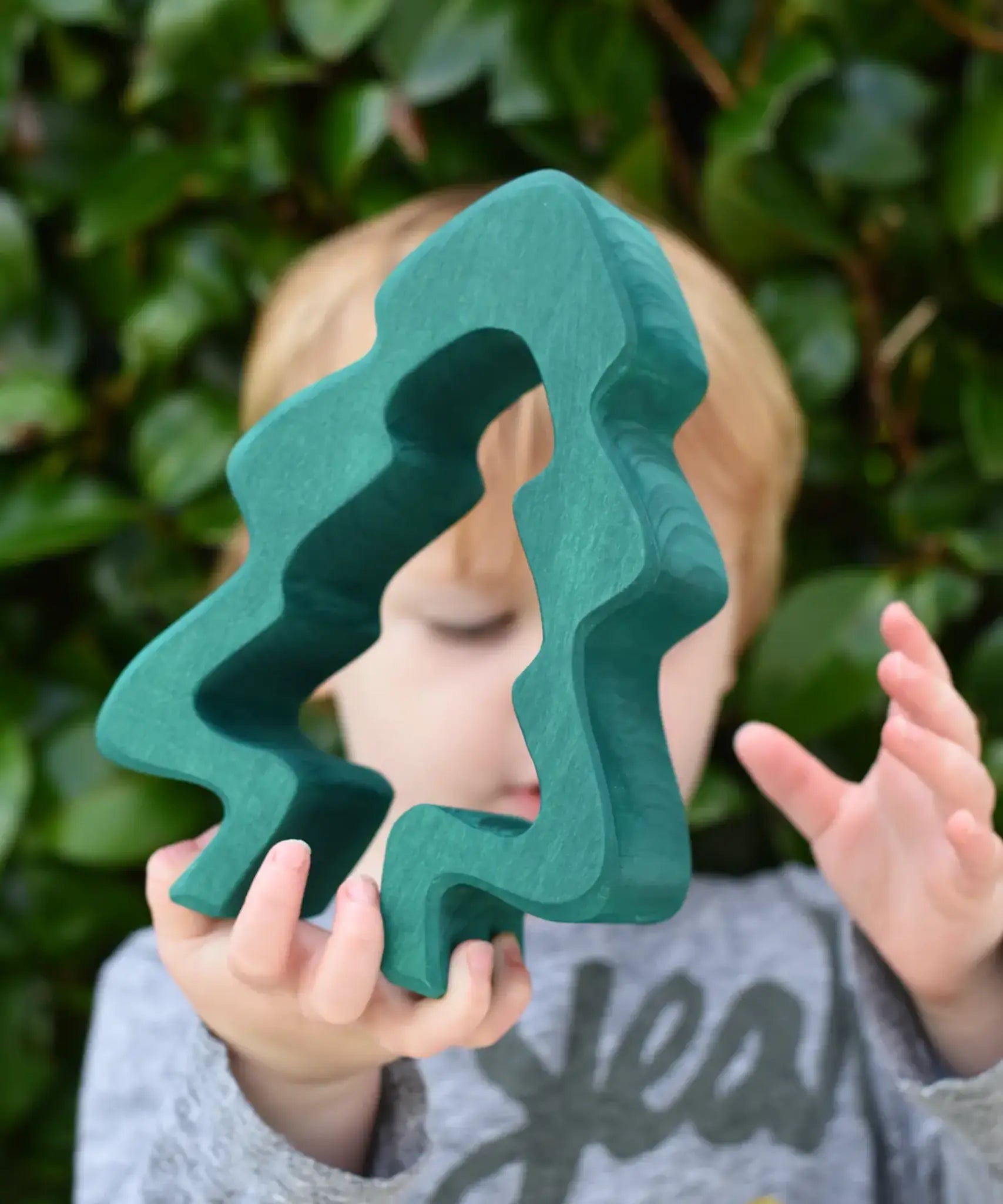 Child holding the large dark green pieces from the Glückskäfer 6-Piece Fir Tree wooden tree stacking toy.