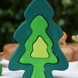 Glückskäfer 6-Piece Fir Tree wooden tree stacking toy with six nested tree shapes in shades of green placed on a wooden surface outdoors.
