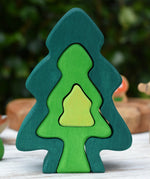 Glückskäfer 6-Piece Fir Tree wooden tree stacking toy with six nested tree shapes in shades of green placed on a wooden surface outdoors.