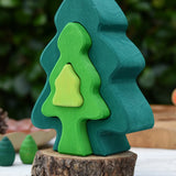 Glückskäfer 6-Piece Fir Tree wooden tree stacking toy with six nested tree shapes in shades of green placed on a log slice.