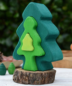 Glückskäfer 6-Piece Fir Tree wooden tree stacking toy with six nested tree shapes in shades of green placed on a log slice.