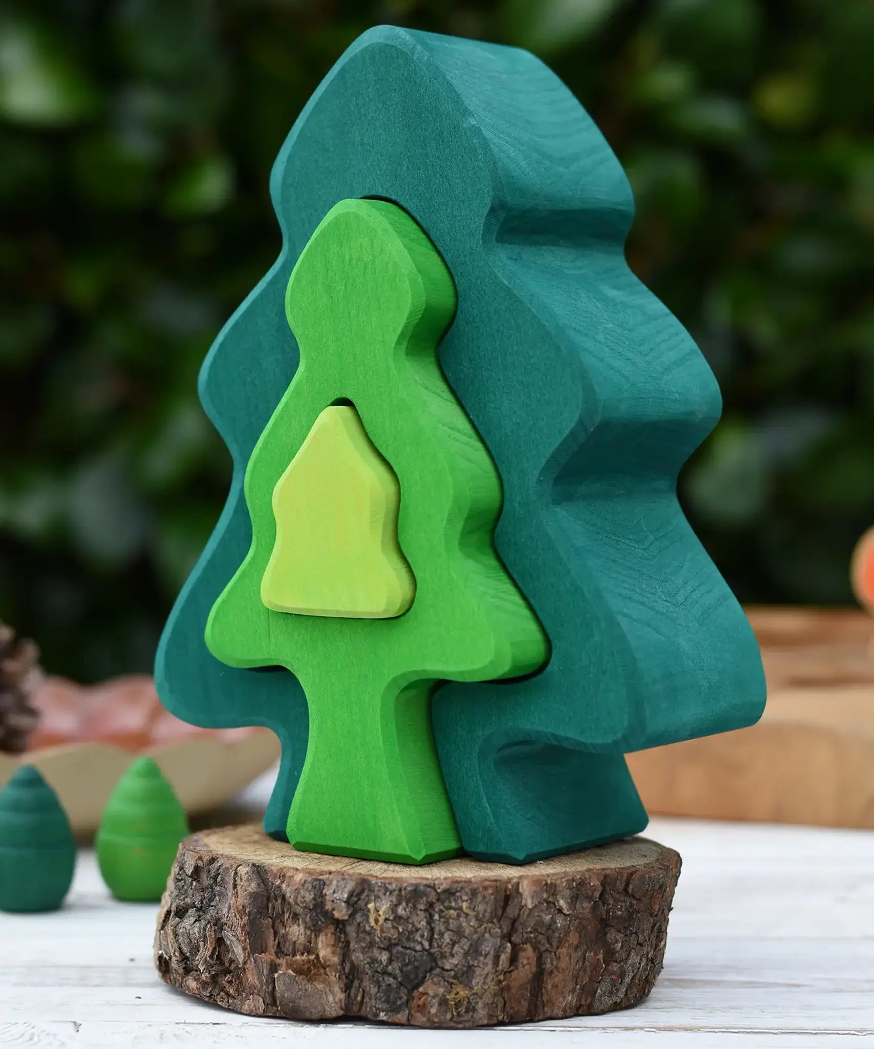 Glückskäfer 6-Piece Fir Tree wooden tree stacking toy with six nested tree shapes in shades of green placed on a log slice.