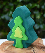 Glückskäfer 6-Piece Fir Tree wooden tree stacking toy with six nested tree shapes in shades of green placed on a wooden surface outdoors.