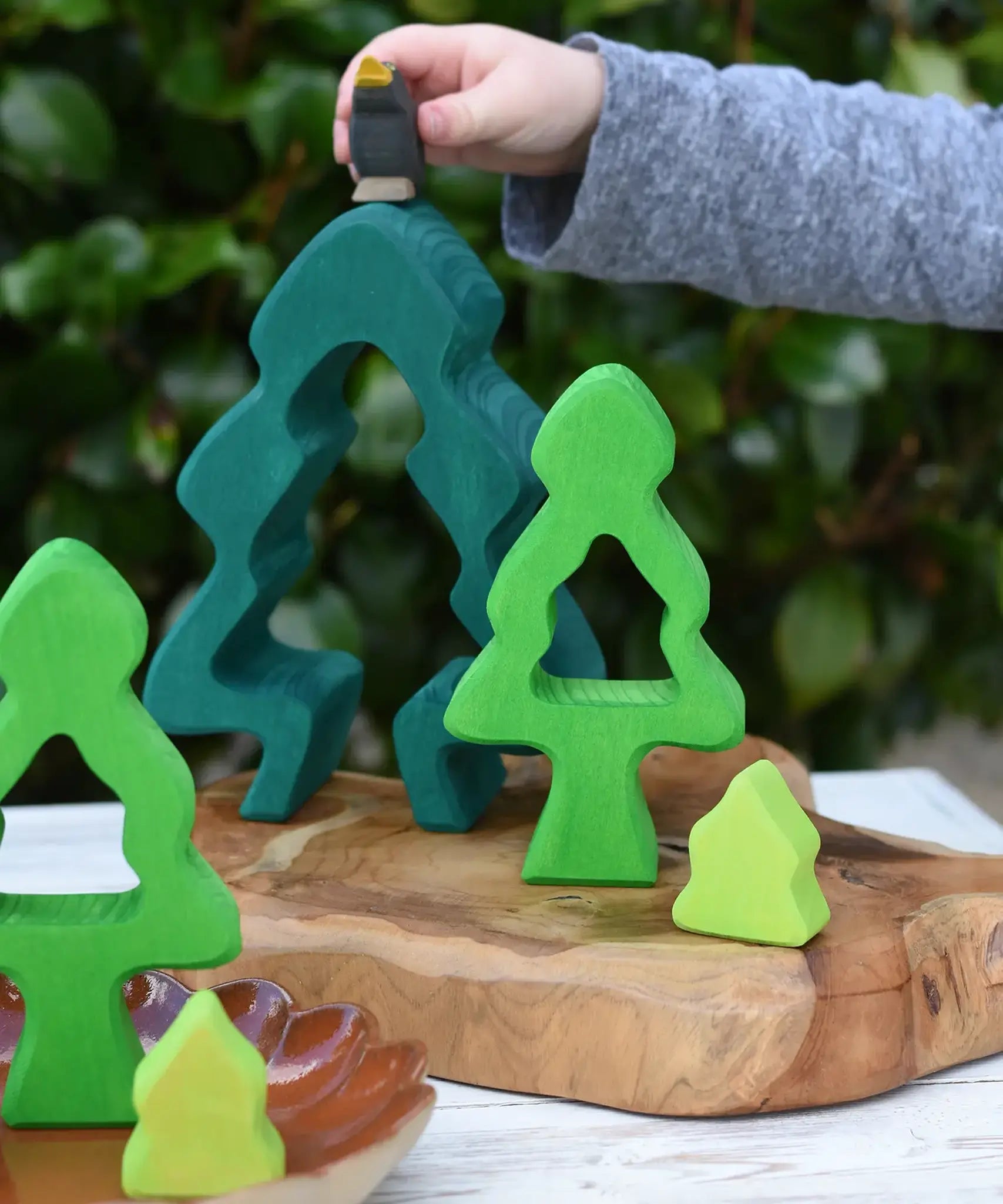 Child playing with the Glückskäfer 6-Piece Fir Tree wooden tree stacking toy holding an Ostheimer blackbird in his hans.