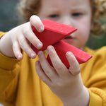 A child holding two red roof shapes blocks in their hands.