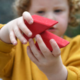A child holding two red roof shapes blocks in their hands.