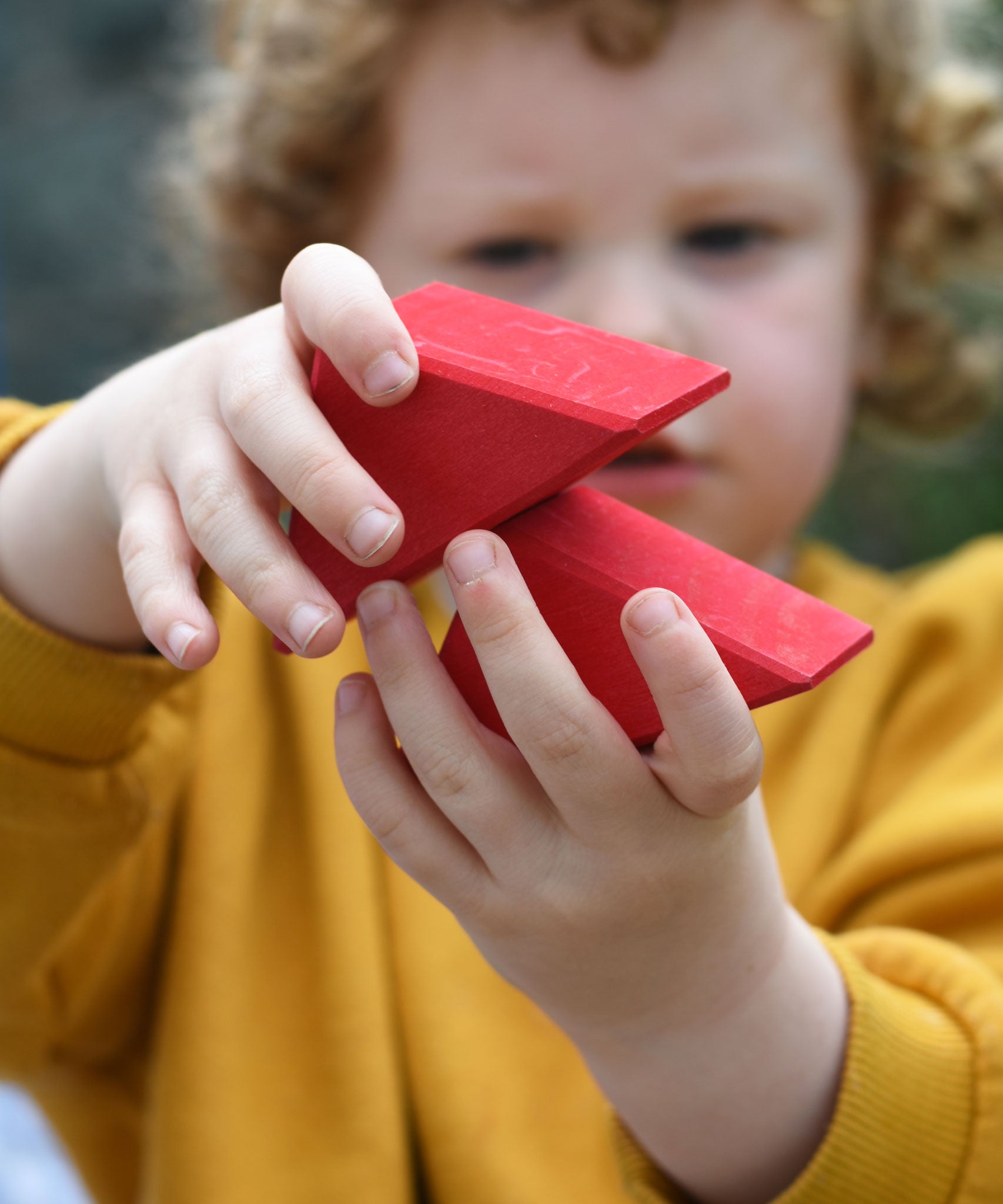 A child holding two red roof shapes blocks in their hands.