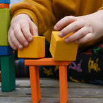 A child placing two yellow cube shaped blocks from the Glückskäfer 29-Piece House Blocks set in a stack.