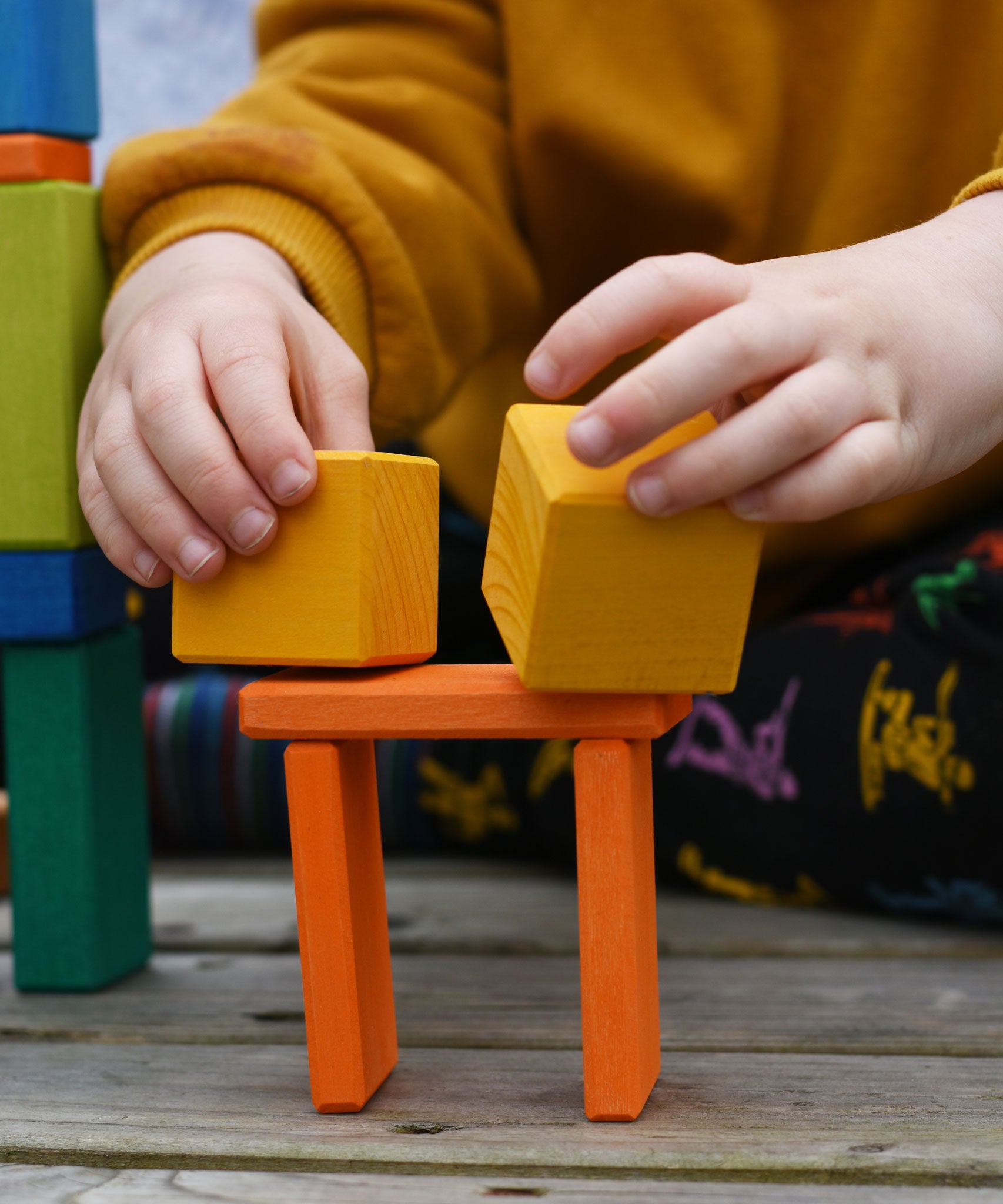 A child placing two yellow cube shaped blocks from the Glückskäfer 29-Piece House Blocks set in a stack.