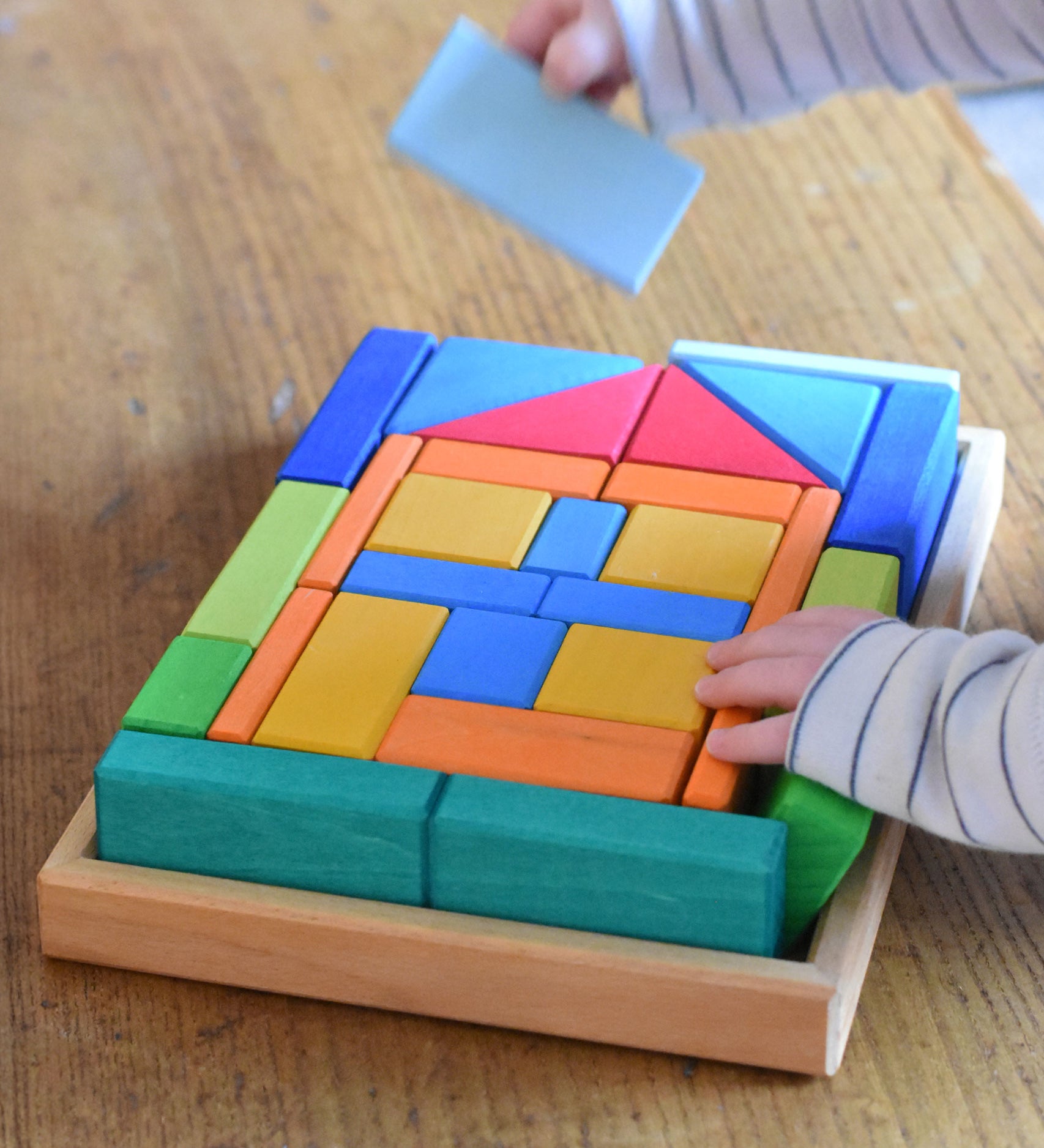 A close up of a young child's hand's taking blocks out of the Glückskäfer 29-Piece House Blocks set tray.