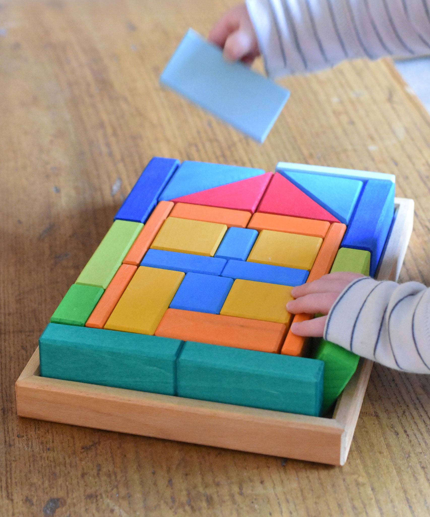 A close up of a young child's hand's taking blocks out of the Glückskäfer 29-Piece House Blocks set tray.
