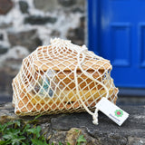 The pieces from the Glückskäfer 23 Piece Wooden Marble Track in theor net storage bag placed on a stone wall outdoors. 