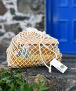 The pieces from the Glückskäfer 23 Piece Wooden Marble Track in theor net storage bag placed on a stone wall outdoors. 