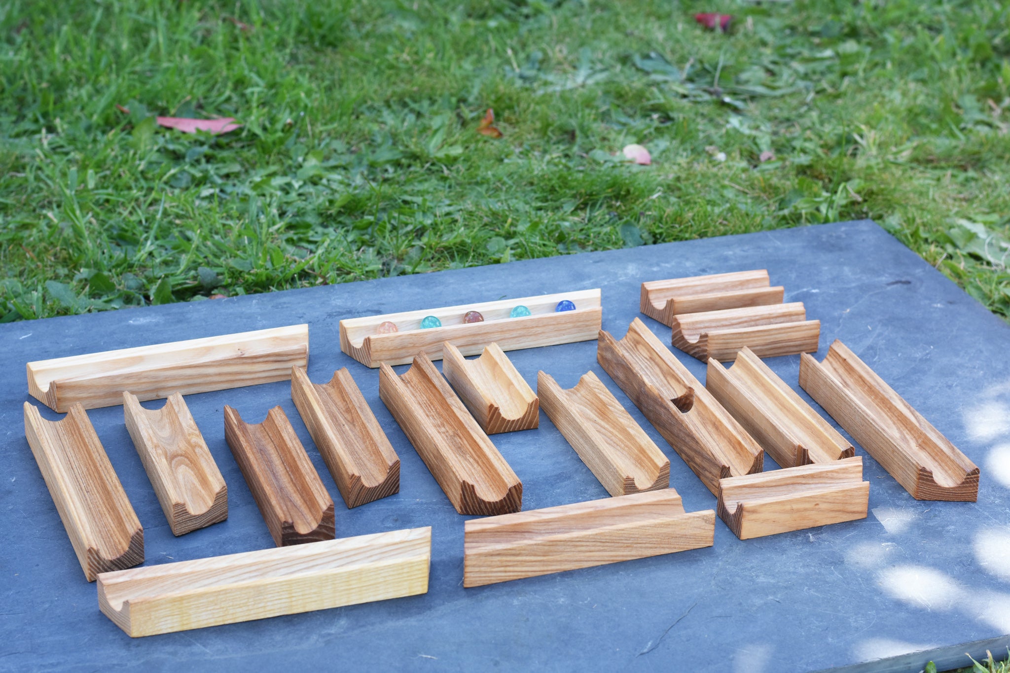 The pieces from the Glückskäfer 23 Piece Wooden Marble Track laid out onto a slate surface outdoors. 