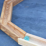 A glass marble placed on the Glückskäfer 23 Piece Wooden Marble Track laid out onto a slate surface outdoors. 