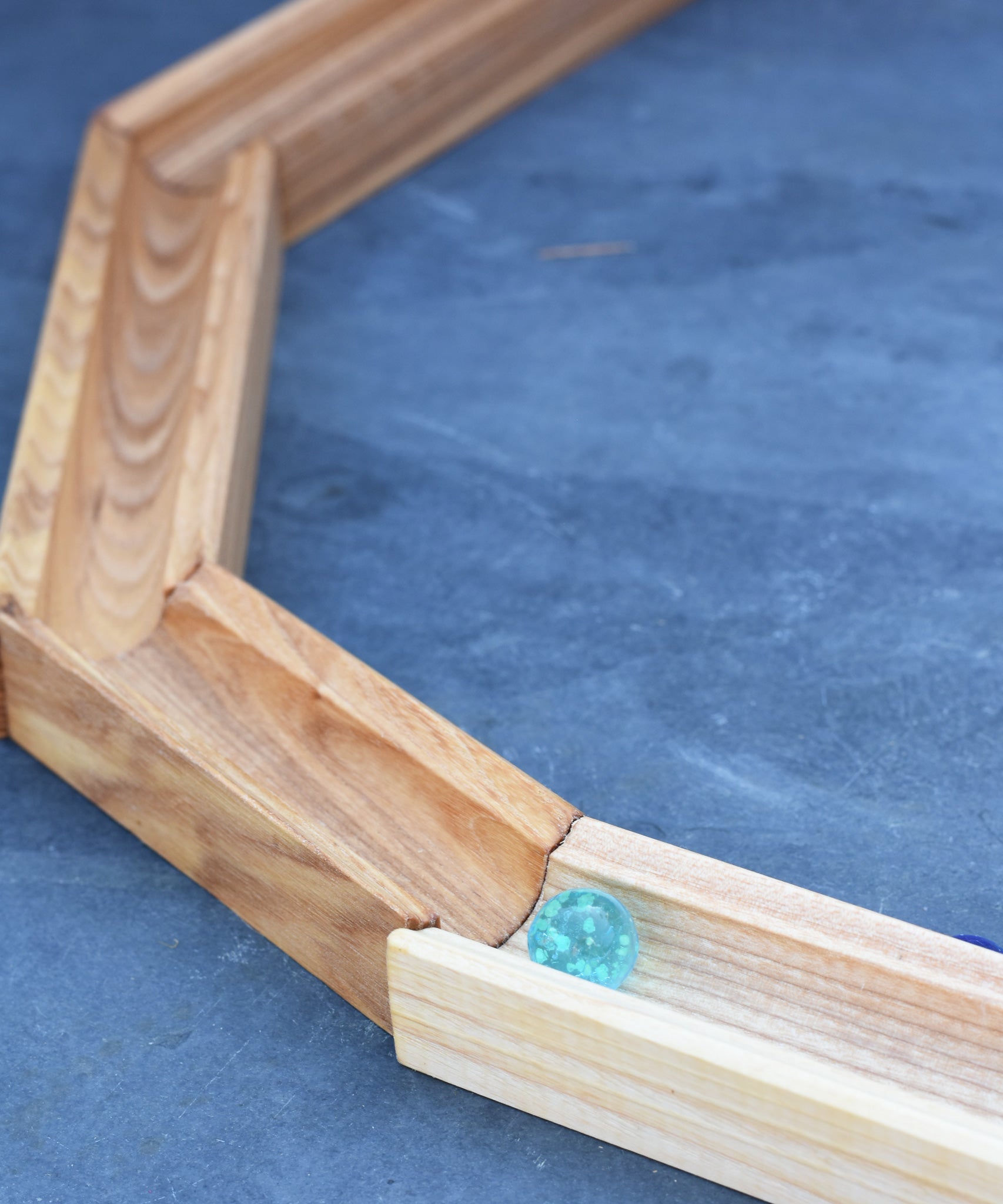 A glass marble placed on the Glückskäfer 23 Piece Wooden Marble Track laid out onto a slate surface outdoors. 