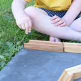 A child placing a glass marble on the Glückskäfer 23 Piece Wooden Marble Track laid out onto a slate surface outdoors. 