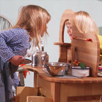 Two children interacting through the double-sided Gluckskafer wooden play kitchen island during imaginative role play.