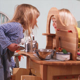 Two children interacting through the double-sided Gluckskafer wooden play kitchen island during imaginative role play.