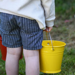A close up of a Glückskäfer Yellow Metal Bucket in a child's hand.