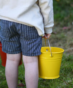 A close up of a Glückskäfer Yellow Metal Bucket in a child's hand.