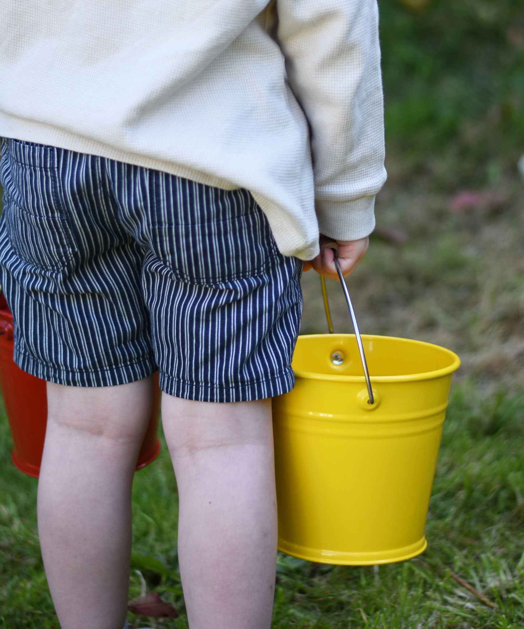 A close up of a Glückskäfer Yellow Metal Bucket in a child's hand.