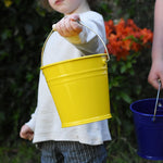 A child holding a Glückskäfer Yellow Metal Bucket in their hand.