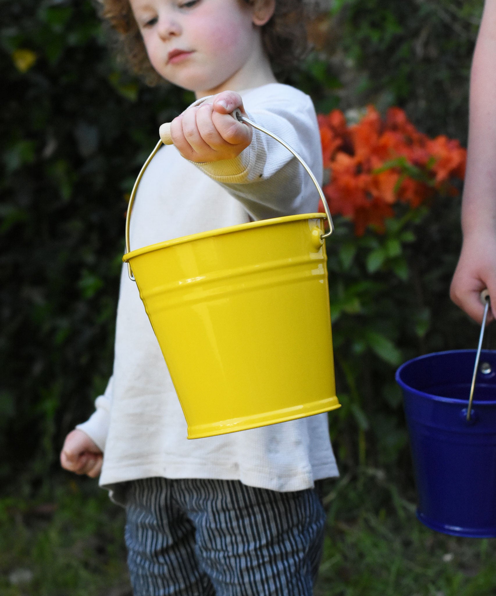 A child holding a Glückskäfer Yellow Metal Bucket in their hand.