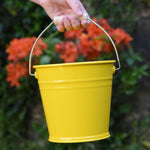 A close up of the Glückskäfer Yellow Metal Bucket in a child's hand. 