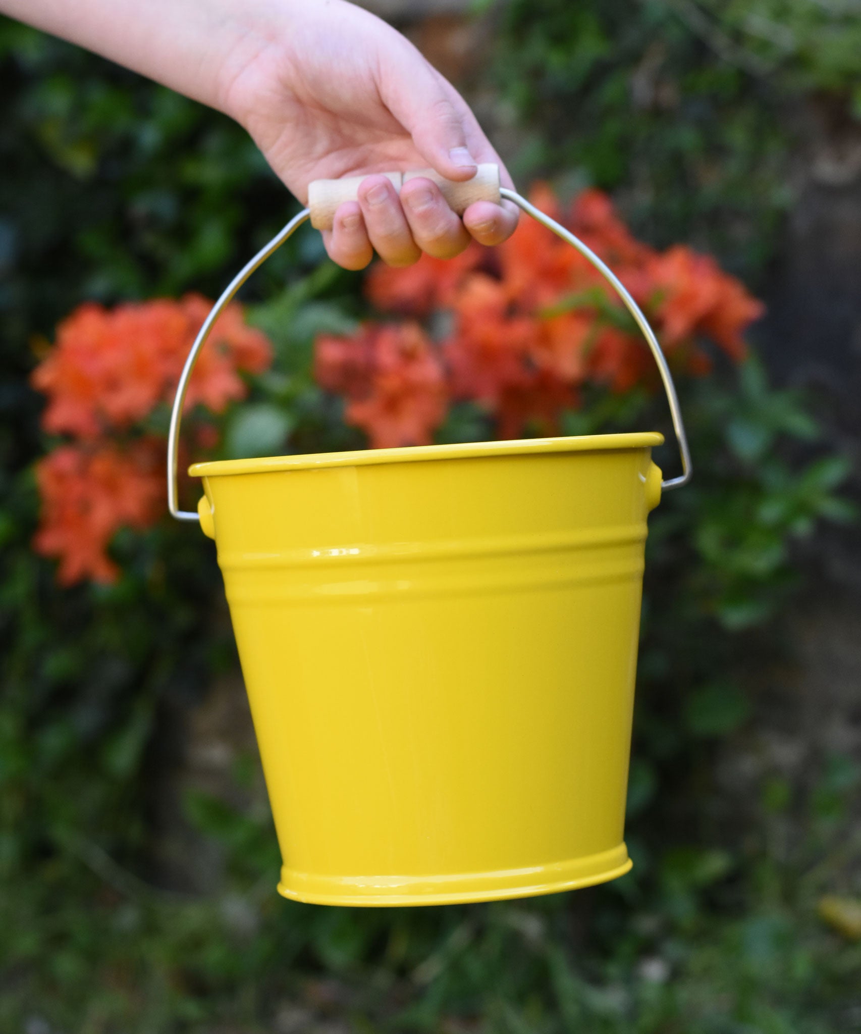 A close up of the Glückskäfer Yellow Metal Bucket in a child's hand. 
